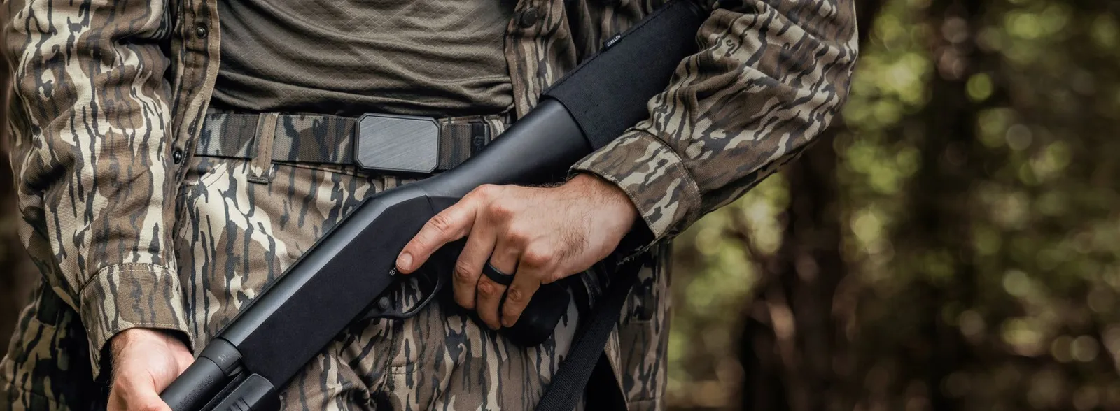 Camo Belt worn by a hunter in woodland camouflage holding a shotgun