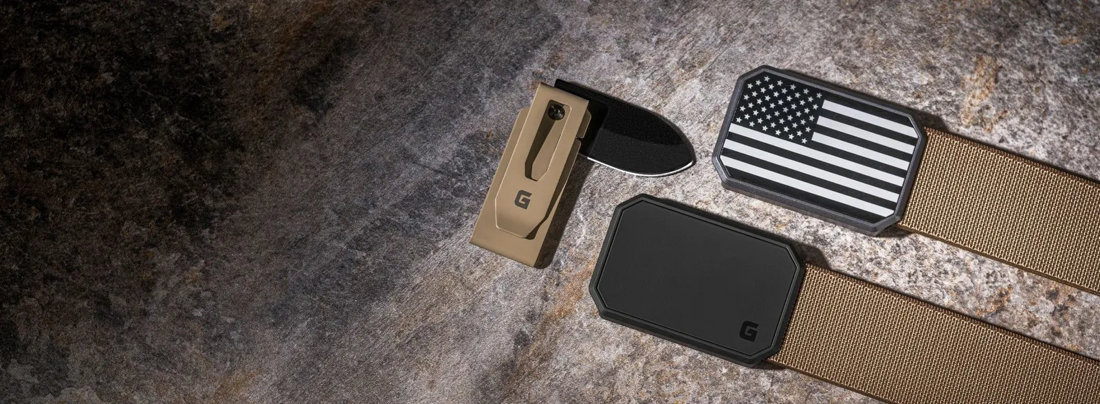Coyote brown Groove Belt with a flag buckle, a coyote money clip knife and a wallet laid on stone