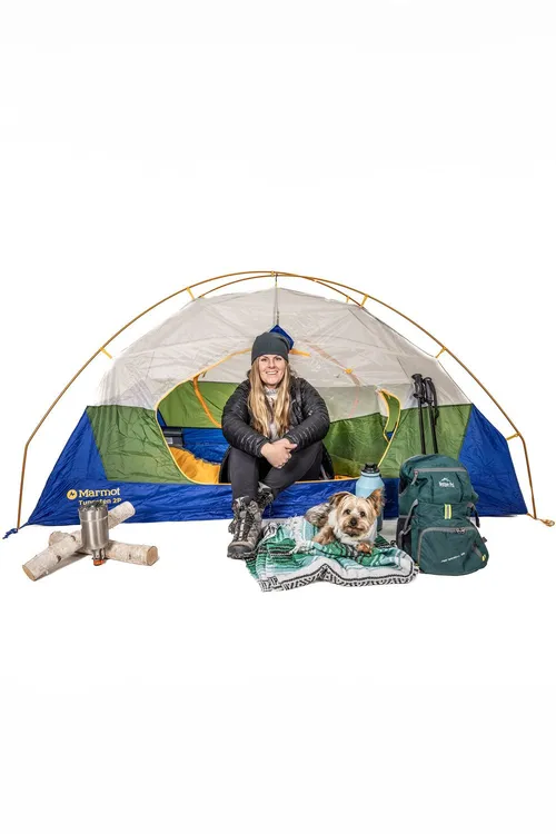 A Groove Life team member sitting in a small tent with a dog and camping gear