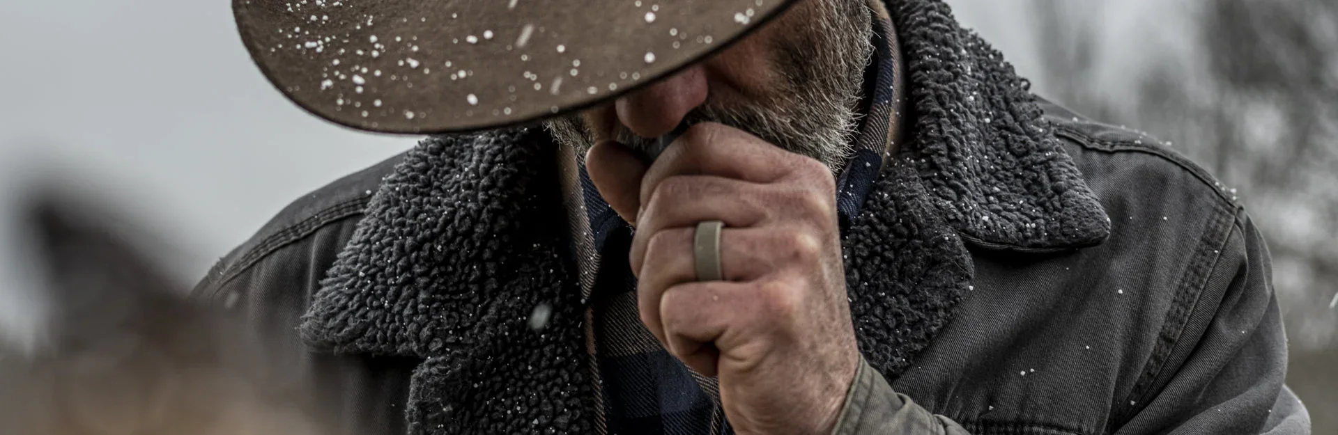 A man in a worn hat and shearling coat, hand to his face, wearing a Groove ring