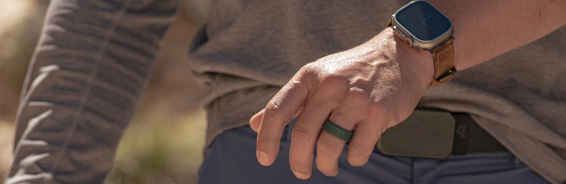 A hand resting on a hip, wearing a Groove ring and an Apple Watch on a brown Groove band
