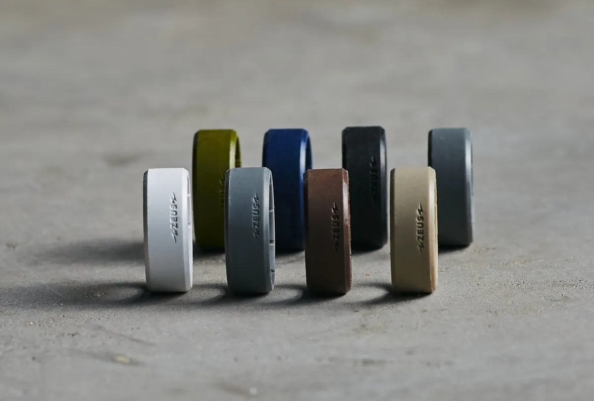 Nine Groove silicone rings standing in a row on concrete, in white, olive, navy, black, brown, tan and grey