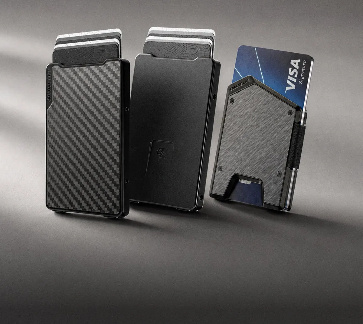 Three Groove Wallets standing in a row: carbon fiber, midnight black and gun metal with cards fanned out